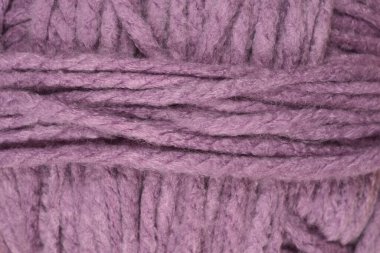 Bir makro çekim yumuşak mor yün yumağının detaylı dokusunu gösterir kalın iç içe geçmiş ipliklerle tüm çerçeveyi doldurur