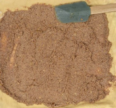 Geleneksel ceviz rulosu hazırlamak için taze maya hamurunu dolduran kalın bir tabaka tatlı ceviz serpiştiren ahşap bir spatula manzarası.