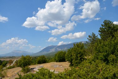 Peruca Gölü 'nün doğu kıyısından geniş bir panoramik manzara, mavi bir yaz gökyüzünün altındaki Dinara dağ sırasının uzak tepelerine bakıyor.