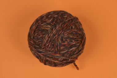 Katı turuncu bir yüzeye yerleştirilmiş kahverengi ve turuncu tonlarda büyük bir yün yumağının üst görüntüsü