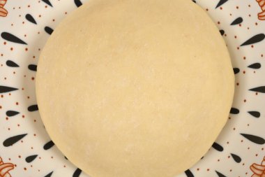 Pürüzsüz yuvarlak bir pizza hamuru topunun beyaz seramik tabakta siyah ve kahverengi desenli desenleri gösteren makro görüntüsü.