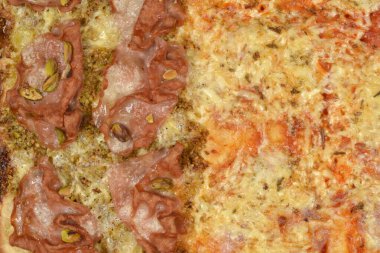 Üstünde çıtır çıtır Mortadella dilimleri olan fırınlanmış bir pizzanın makro görüntüsü yeşil şam fıstığı ve erimiş altın peynir tüm çerçeveyi iştah açıcı dokularla dolduruyor.