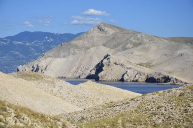 Prvic adasının çorak ve kayalık manzarası açık bir yaz gökyüzünün altında Krk adasından mavi denizin karşısında görülüyor.