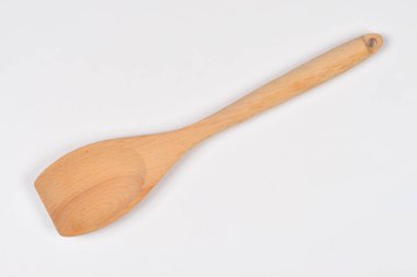 Yemek pişirmek ve karıştırmak için kullanılan düz beyaz bir yüzey üzerinde köşegen şeklinde uzanan tek bir açık kahverengi ahşap spatula manzarası.