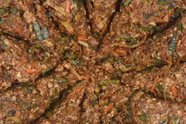 Kömür ve ince doğranmış sebzelerden oluşan koyu ve baharatlı bir karışımın yakın plan görüntüsü, muhtemelen yuvarlak bir desen içinde yerleştirilmiş hamur köftesi veya köfte için bir dolgu.