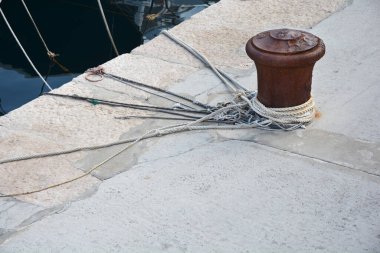 Etrafına birkaç denizcilik halatı bağlanmış paslı bir demir korkuluk karanlık suyun yanındaki bir taş iskelede duruyor..