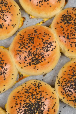 Yüksek açılı, siyah susamlı kahverengi hamburger çörekleri ve beyaz parşömen kağıdının üzerinde parlak bir yumurta jölesi.