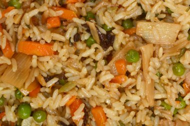 Bezelye havucu, mantar ve küçük kızarmış domuz parçaları ile karıştırılmış pilav detaylı bir yakın plan.