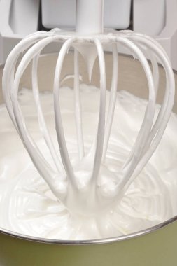 Mutfakta tatlı hazırlarken içi kalın, parlak, beyaz, çırpılmış krema karışımıyla dolu yeşil bir tezgah karıştırıcı kasesi.