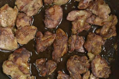 Koyu bir tavada yağda kızartılmış birkaç parça kızarmış tavuk ciğeri.