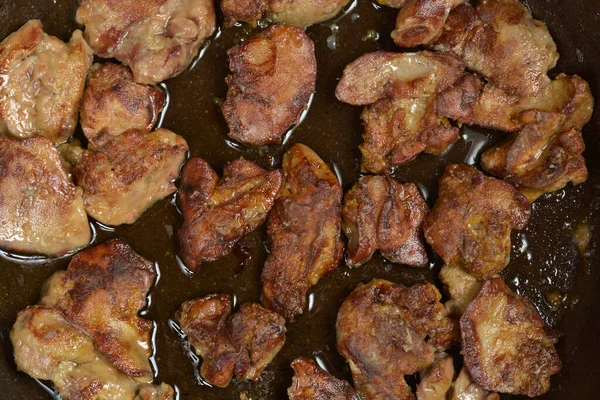 Koyu bir tavada yağda kızartılmış birkaç parça kızarmış tavuk ciğeri.
