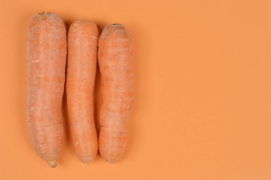 Üç adet soyulmamış turuncu havuç dikey olarak turuncu bir yüzeye yerleştirilmiş ve sağ tarafta fotokopi alanı var.