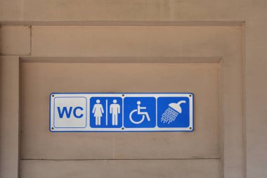 Erkekler ve kadınlar için tuvaletin yerini gösteren mavi ve beyaz bir işaret ve bej bir duvardaki duş tesisi.