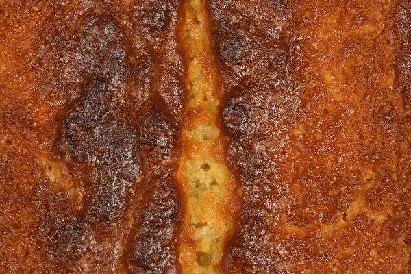 Fırınlanmış limonlu kekin altın kahverengi kabuğunun tam kare makro görüntüsü tatlı tatlıların gözenekli ve dokulu yüzeyini içerir.