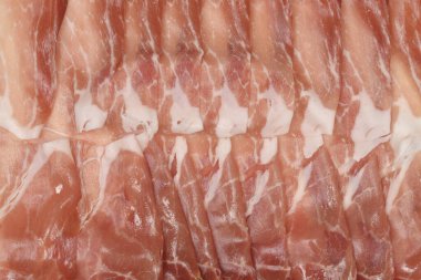 Yağlı ve kırmızı et liflerinin mermer dokusunu gösteren kuru jambon dilimlerinin birkaç ince diliminin makro görüntüsünü kapat.