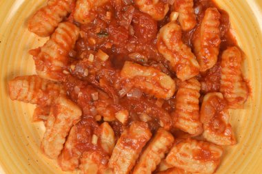 Süzme peynir ve unla kaplanmış sarı tabakta domates sosuyla ev yapımı gnocchi 'nin detaylı bir fotoğrafı.