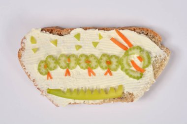 Kereviz ve havuçla süslenmiş beyaz krem peynirli bir dilim ekmek beyaz arka planda yeşil tırtıla benzesin diye.