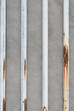 Gri desenli bir yüzey üzerinde sıralanmış pas lekeleri olan dikey beyaz metal çubukların üst görüntüsü
