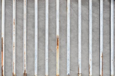 Görünür pas lekeleri ve aşınması olan birden fazla dikey beyaz metal çubuğun düz bir görünümü var.