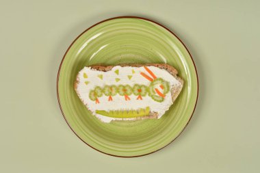 Krem peynirli ve yeşil tabakta sebzelerden yapılmış tırtıllı yaratıcı bir sandviç.