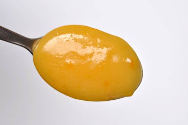 Tarafsız açık gri bir arkaplanda gümüş bir kaşığa tutulmuş pürüzsüz ve parlak turuncu bir kaymak resmi.