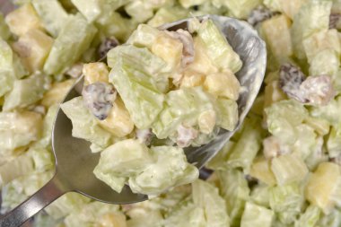 Metal kaşık içinde bol miktarda kremalı Waldorf salatası bulunur. Kereviz sapından, elma sapından, kuru üzümden ve mayonezli cevizden yapılmıştır..