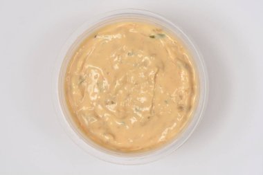 Beyaz arka planda şeffaf plastik bir kasede servis edilen küçük yeşil bitkilerle kaplı kremalı somon balığının üst görüntüsü.