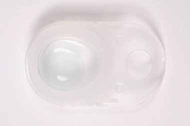 Yumuşak bir lensin üst görüntüsü, beyaz bir zemin üzerinde temiz bir plastik kabarcık paketinin içinde sıvıya batırılmış.
