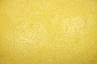 Detaylı bir makro çekim, küçük gözenekleri ve ince yüzey değişimlerini gösteren taze bir limonun dokulu sarı derisini yakalar..