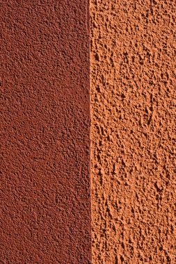 Dikey bileşim koyu kırmızımsı kahverengi ile turuncu desenli alçı duvar yüzeyi arasında parlak güneş ışığı altında pürüzlü bir tahıl bitişiyle keskin bir kontrastı gösteriyor.