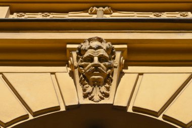 Klasik sarı bina cephesinde sakallı bir erkek yüzü olan dekoratif bir mimari anahtar taşı.