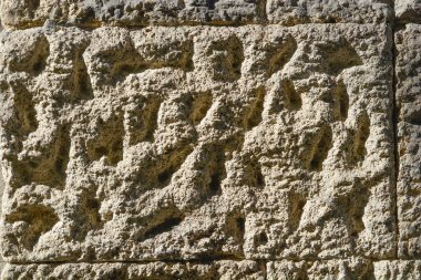 Yakın çekim, parlak güneş ışığı altında derin gözenekli delikleri ve doğal dokuları olan eski bir taş bloğun pürüzlü ve yıpranmış yüzeyini gösteriyor.