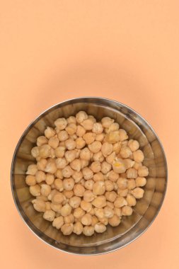 Kurumuş bezelyelerin, paslanmaz çelik bir kasenin içinde, temiz, beyaz bir arka planı olan, suya batırılmış, tepeden tırnağa görüntüsü.