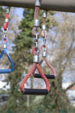Açık hava oyun alanındaki metal bir bardan sallanan siyah plastik saplı kırmızı tırmanma halatlarının yakın plan fotoğrafı.