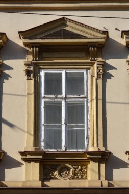 Dekoratif taş çerçeveli eski beyaz ahşap bir pencere klasik süslemeler ve bej bir bina duvarında üçgen bir pedikür.
