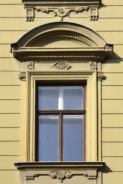 Klasik ahşap bir pencere özenle hazırlanmış taş oymalar ve yatay çizgili sarı bir binanın ön cephesinde eğri bir pedikürle çerçevelenir.