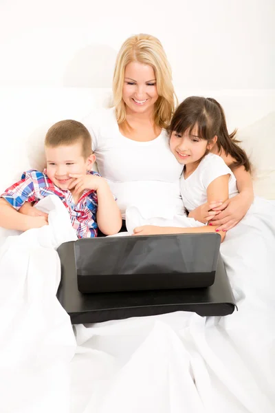Moeder met haar kinderen met behulp van een laptop in bed — Stockfoto