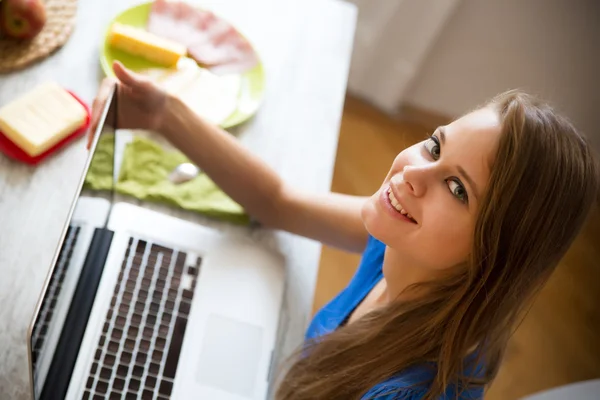 Ung kvinna äter frukost medan du använder en bärbar dator — Stockfoto