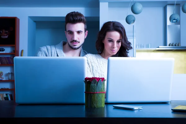 Casal jovem na frente de seus computadores portáteis em casa — Fotografia de Stock