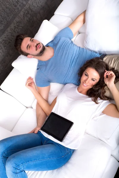 Νεαρό ζευγάρι που χρησιμοποιούν ένα Tablet PC μαζί στον καναπέ στο σπίτι — Φωτογραφία Αρχείου