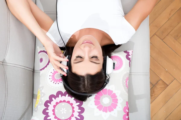 Belle jeune femme allongée sur le canapé écoutant de la musique — Photo