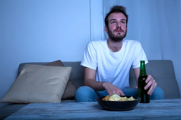 Jonge man kijken Tv bij nacht met chips en bier — Stockfoto