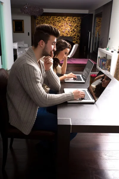 Casal jovem na frente de seus computadores portáteis em casa — Fotografia de Stock