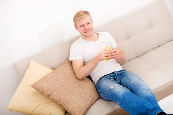 Mladý muž jí sendvič doma — Stock fotografie
