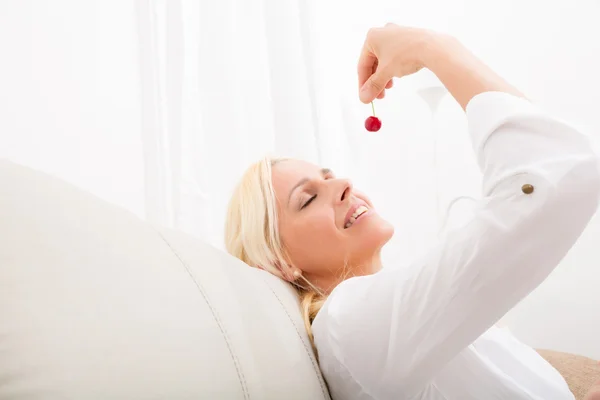 Mulher comendo cereja no sofá — Fotografia de Stock