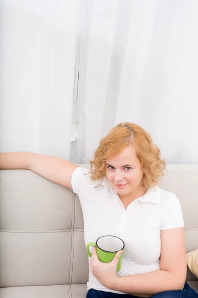 ソファの上にコーヒーのカップを持つ若い女 — ストック写真