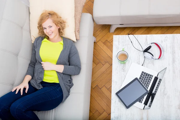 Jonge vrouw op de bank met gadgets — Stockfoto