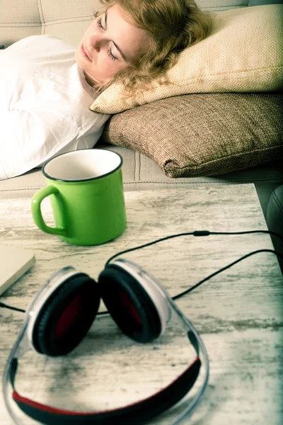 Masanın üzerinde kulaklık ile kanepede uyuyan kadın — Stok fotoğraf