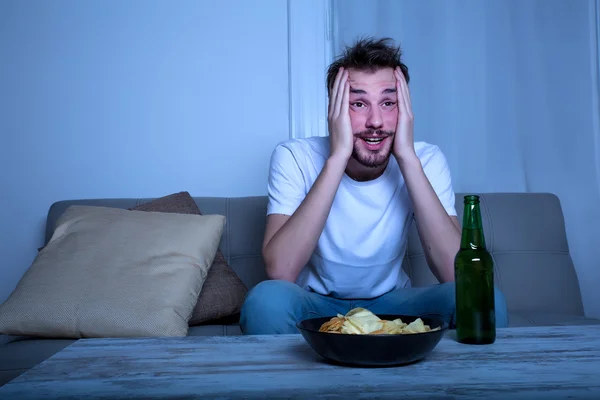 Jovem assistindo TV à noite com batatas fritas e cerveja — Fotografia de Stock