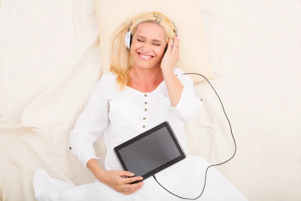 Kvinna med hörlurar och tablet i sängen — Stockfoto